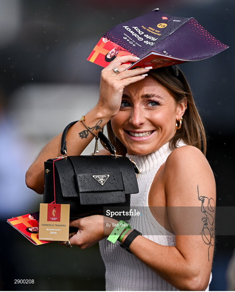 31 July 2024; A racegoer attempts to shelter from the rain during day three of the Galway Races Summer Festival at Ballybrit Racecourse in Galway. Photo by Seb Daly/Sportsfile
