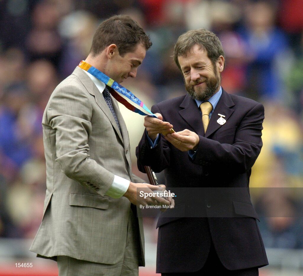 12 September 2004; President of the GAA Sean Kelly, admires the Gold Medal won by Irish Olympic Gold Medallist Cian O'Connor in Athens recently, after making a special presentation to him at half-time. Guinness All-Ireland Senior Hurling Championship Final, Cork v Kilkenny, Croke Park, Dublin. Picture credit; Brendan Moran / SPORTSFILE *** Local Caption *** Any photograph taken by SPORTSFILE during, or in connection with, the 2004 Guinness All-Ireland Hurling Final which displays GAA logos or contains an image or part of an image of any GAA intellectual property, or, which contains images of a GAA player/players in their playing uniforms, may only be used for editorial and non-advertising purposes.  Use of photographs for advertising, as posters or for purchase separately is strictly prohibited unless prior written approval has been obtained from the Gaelic Athletic Association.
