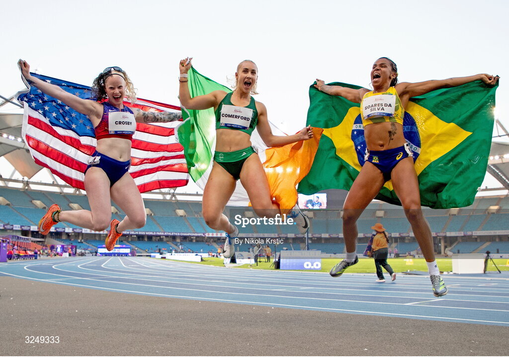 28 September 2025; Orla Comerford of team Ireland, centre, who won gold, Rayane Soares da Silva of Brazil, right, who won silver, and Kym Crosby of USA, who won bronze, celebrate after the Women's T13 100m final during day three of the New Delhi 2025 World Para Athletics Championships at JLN Stadium in New Delhi, India. Photo by Nikola Krstic/Sportsfile