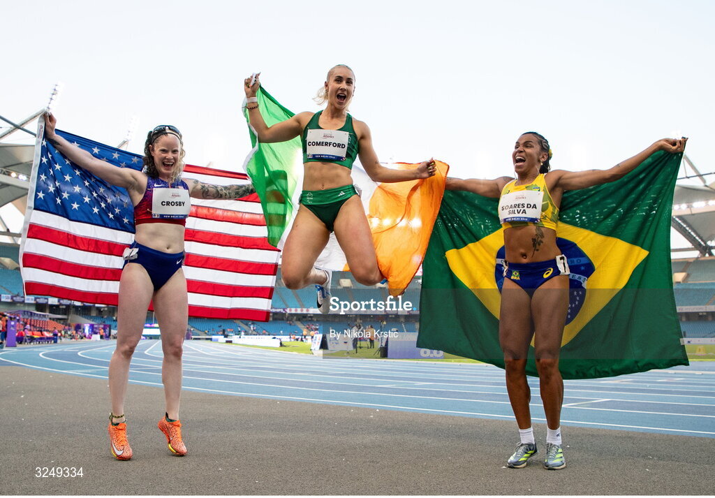 28 September 2025; Orla Comerford of team Ireland, centre, who won gold, Rayane Soares da Silva of Brazil, right, who won silver, and Kym Crosby of USA, who won bronze, celebrate after the Women's T13 100m final during day three of the New Delhi 2025 World Para Athletics Championships at JLN Stadium in New Delhi, India. Photo by Nikola Krstic/Sportsfile