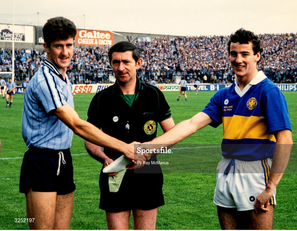 23 September 1984; Dublin captain Paul Clarke shakes hands with Tipperary captain Frank Howlin, in the company of referee Pádraig Hughes, before the All Ireland Minor Football Final match between Dublin and Tipperary at Croke Park, Dublin. Photo by Ray McManus/Sportsfile