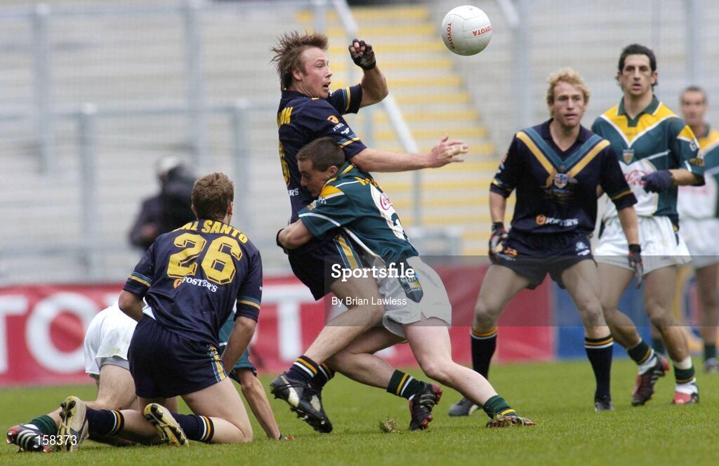 17 October 2004; Max Hudghton, Australia, is tackled by Ireland's Brian McGuigan, as team-mate Nick Dal Santo (26) looks on. Coca Cola International Rules Series 2004, First Test, Ireland v Australia, Croke Park, Dublin. Picture credit; Brian Lawless / SPORTSFILE *** Local Caption *** Any photograph taken by SPORTSFILE during, or in connection with, the 2004 Coca Cola International Rules Series which displays GAA logos or contains an image or part of an image of any GAA intellectual property, or, which contains images of a GAA player/players in their playing uniforms, may only be used for editorial and non-advertising purposes.  Use of photographs for advertising, as posters or for purchase separately is strictly prohibited unless prior written approval has been obtained from the Gaelic Athletic Association.