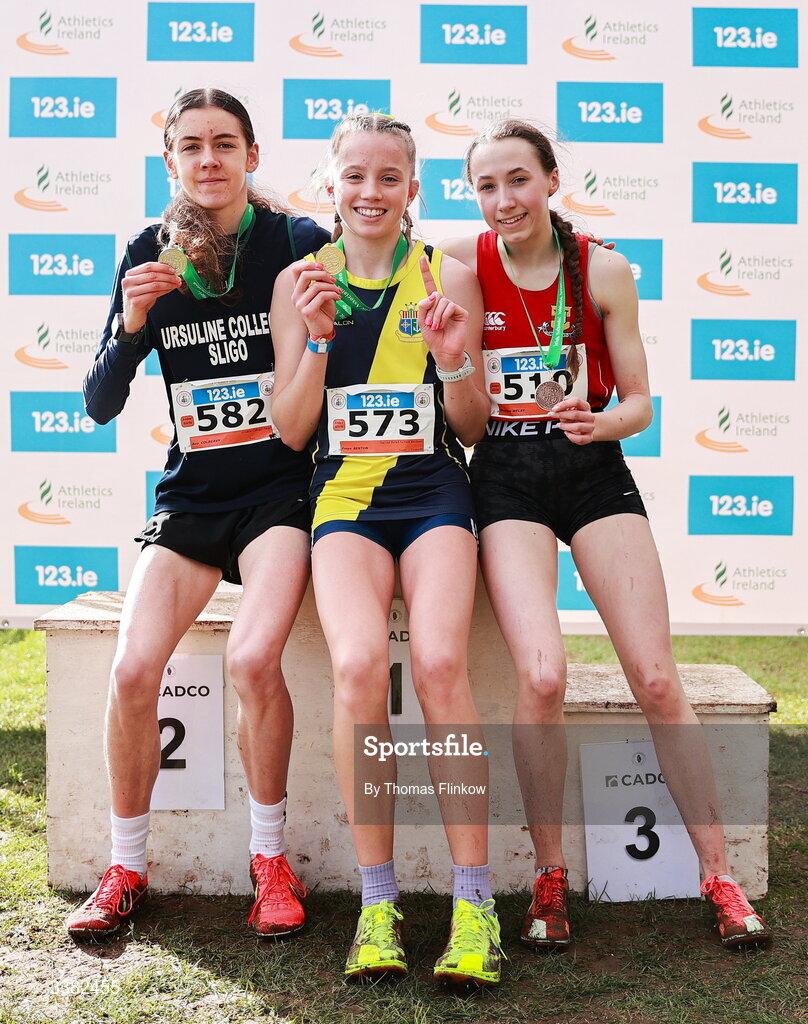 7 March 2026; Gold medalist Freya Renton of Sacred Heart School Westport, Mayo, with Ava Colreavy of Ursuline College, Sligo, left, and Madison Welby of Friends' School Lisburn, Antrim after the inter girls event during the 123.ie All Ireland Schools’ Cross Country Championships at Mallusk Playing Fields in Newtownabbey, Antrim. Photo by Thomas Flinkow/Sportsfile
