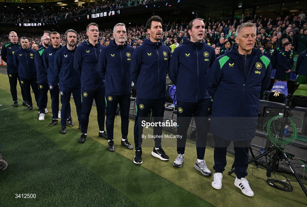 31 March 2026; Republic of Ireland head coach Heimir Hallgrimsson with coaches and backroom staff, from right, assistant head coach John O'Shea, assistant coach Paddy McCarthy, goalkeeping coach Gudmundur Hreidarsson, head of athletic performance Damien Doyle, team doctor Sean Carmody, lead physiotherapist Danny Miller, kit and equipment manager Karl McKenna, physiotherapist Cian McCaffrey and sports scientist Adam Fox stand for the playing of the National Anthem before the international friendly match between Republic of Ireland and North Macedonia at Aviva Stadium in Dublin. Photo by Stephen McCarthy/Sportsfile