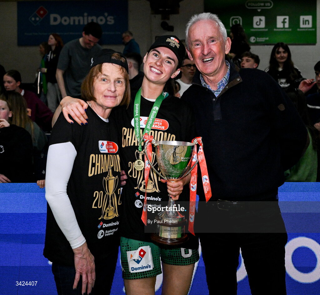 12 April 2026; The captain of Trinity Meteors, Catherine Connaire, centre, celebrates with the cup with her parents, Mags Connaire, left and Barry Connaire, right, after the Basketball Ireland Women's Superleague final match between Trinity Meteors and UCC Glanmire at the National Basketball Arena in Tallaght, Dublin. Photo by Paul Phelan/Sportsfile