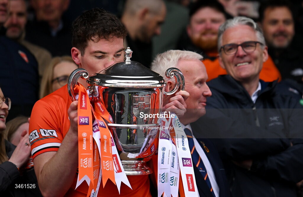 17 May 2026; Jarly Og Burns of Armagh, watched by his dad, and Uachtarán Chumann Lúthchleas Gael Jarlath Burns, lifts the Anglo Celt Cup after the Ulster GAA Football Senior Championship final match between Armagh and Monaghan at St Tiernach's Park in Clones, Monaghan. Photo by Ramsey Cardy/Sportsfile