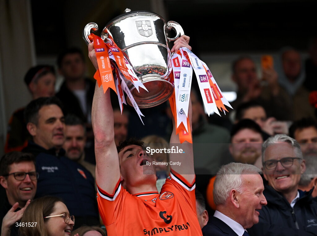 17 May 2026; Jarly Og Burns of Armagh, watched by his dad, and Uachtarán Chumann Lúthchleas Gael Jarlath Burns, lifts the Anglo Celt Cup after the Ulster GAA Football Senior Championship final match between Armagh and Monaghan at St Tiernach's Park in Clones, Monaghan. Photo by Ramsey Cardy/Sportsfile