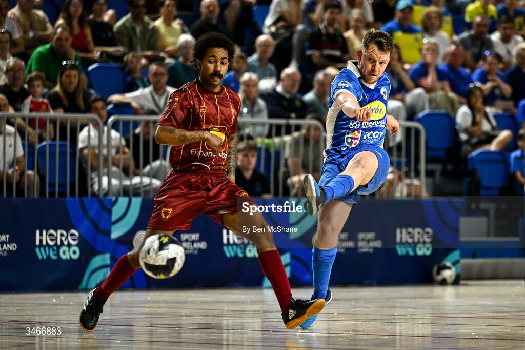 24 May 2026; Ian Byrne of Blue Magic scores his side's third goal despite the tackle of Wemerson Moutinho Dos Santos of Leinster Futsal during the FAI Futsal Cup final match between Leinster Futsal and Blue Magic at the National Indoor Arena in Abbotstown, Dublin. Photo by Ben McShane/Sportsfile