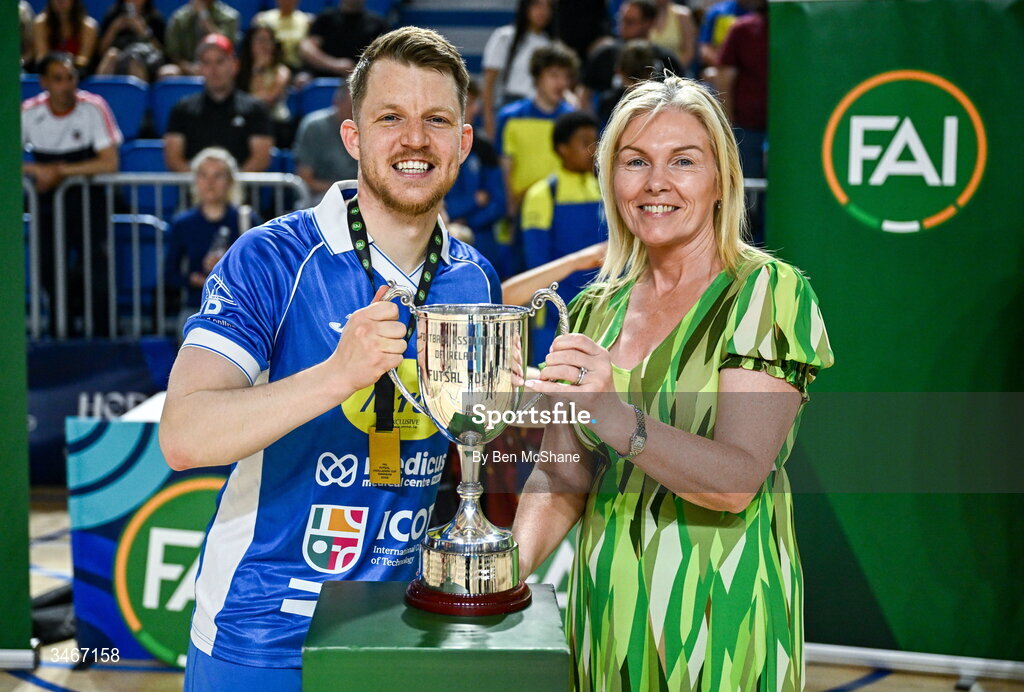 24 May 2026; Blue Magic captain Ian Byrne is presented the cup by FAI board members Caroline Rattigan after the FAI Futsal Cup final match between Leinster Futsal and Blue Magic at the National Indoor Arena in Abbotstown, Dublin. Photo by Ben McShane/Sportsfile
