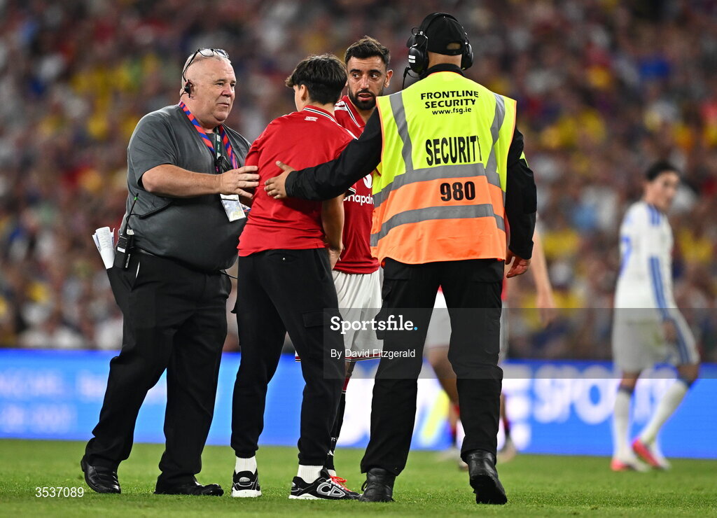 12 August 2026; A pitch invader is escorted off the pitch by stewards as Bruno Fernandes of Manchester United looks on during the pre-season friendly match between Manchester United and Leeds United at Croke Park in Dublin. Photo by David Fitzgerald/Sportsfile
