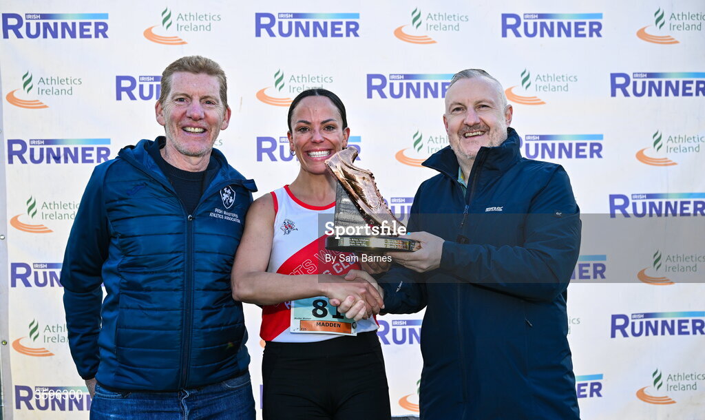 18 October 2026; Lisa Madden of Sportsworld AC, Dublin, is presented with the Jim McNamara Trophy by Irish Masters Athletics Association President Ronan Gately, left, and Shane McNamara, right, after winning the Master Women 6000m during the Autumn Open Cross Country International at the Sport Ireland Campus in Dublin. Photo by Sam Barnes/Sportsfile