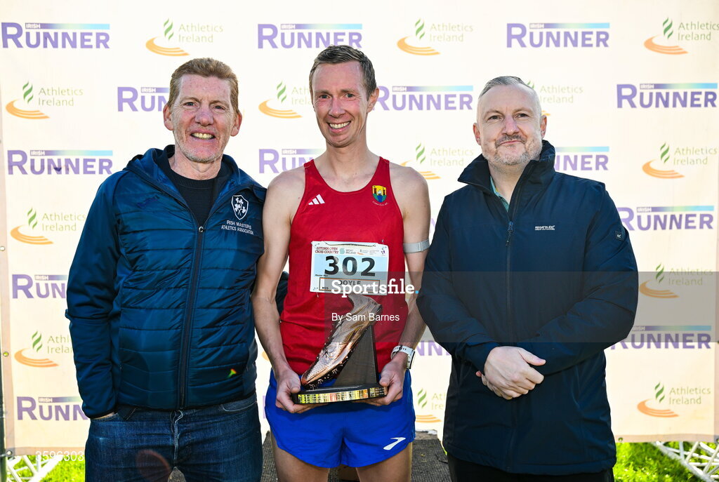 18 October 2026; Sean Doyle of Cork City AC is presented with the Jim McNamara Trophy by Irish Masters Athletics Association President Ronan Gately, left, and Shane McNamara, right, after winning the Master Men 7500m during the Autumn Open Cross Country International at the Sport Ireland Campus in Dublin. Photo by Sam Barnes/Sportsfile