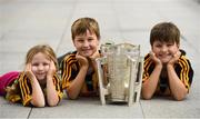 16 August 2019; The Heinrich family, from left, 5 year old Róisín, 8 year old Cillian, and 10 year old Cormac, living in Sevenoaks, Kent, England, originally from Kells, Kilkenny, with the Liam MacCarthy Cup at the GAA’s Home for the Match stand in the arrivals hall at Dublin Airport. Photo by Ramsey Cardy/Sportsfile