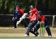 28 July 2022; Curtis Campher of Munster Reds plays a shot watched by Northern Knights wicketkeeper Neil Rock during the Cricket Ireland Inter-Provincial Trophy match between Munster Reds and Northern Knights at Pembroke Cricket Club in Dublin. Photo by Sam Barnes/Sportsfile