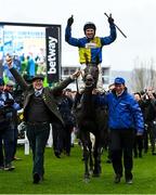 15 March 2023; Jockey Harry Skelton celebrates on Lander Dan after winning the Coral Cup Handicap Hurdle, as they are led into the winners enclosure by owner Colm Donlon, left, and groom Stephen Petch, right, during day two of the Cheltenham Racing Festival at Prestbury Park in Cheltenham, England. Photo by Harry Murphy/Sportsfile