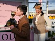 14 March 2025; Jake Cromwell, son of winning trainer Gavin Cromwell, kisses the Boodles Cheltenham Gold Cup, watched by Kiva Cromwell, after they sent out Inothewayurthinkin to win the Boodles Cheltenham Gold Cup Steeple Chase on day four of the Cheltenham Racing Festival at Prestbury Park in Cheltenham, England. Photo by David Fitzgerald/Sportsfile