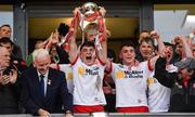 28 May 2025; Tyrone captain Joey Clarke, centre, lifts the trophy, presented by Ulster Council Chairman Michael Geoghegan, left, after his side's victory in the Dalata Hotel Group GAA Football All-Ireland U20 Championship final match between Louth and Tyrone at BOX-IT Athletic Grounds in Armagh. Photo by Oliver McVeigh/Sportsfile