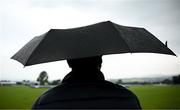 12 June 2025; A spectator waits under an umbrella before match one of the T20 International Series between Ireland and the West Indies at Bready Cricket Club in Magheramason, Tyrone. Photo by Seb Daly/Sportsfile