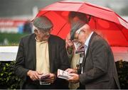 30 July 2014; A general view of racegoers sheltering under an umberella in the wet conditions as they look up the form during the days races. Galway Racing Festival, Ballybrit, Co. Galway. Picture credit: Barry Cregg / SPORTSFILE