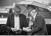 30 July 2014; (Editors please note; This black & white image has been created from an original colour file) A general view of racegoers sheltering under an umberella in the wet conditions as they look up the form during the day's races. Galway Racing Festival, Ballybrit, Co. Galway. Picture credit: Barry Cregg / SPORTSFILE