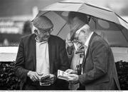 30 July 2014; (Editors please note; This black & white image has been created from an original colour file) A general view of racegoers sheltering under an umberella in the wet conditions as they look up the form during the day's races. Galway Racing Festival, Ballybrit, Co. Galway. Picture credit: Barry Cregg / SPORTSFILE